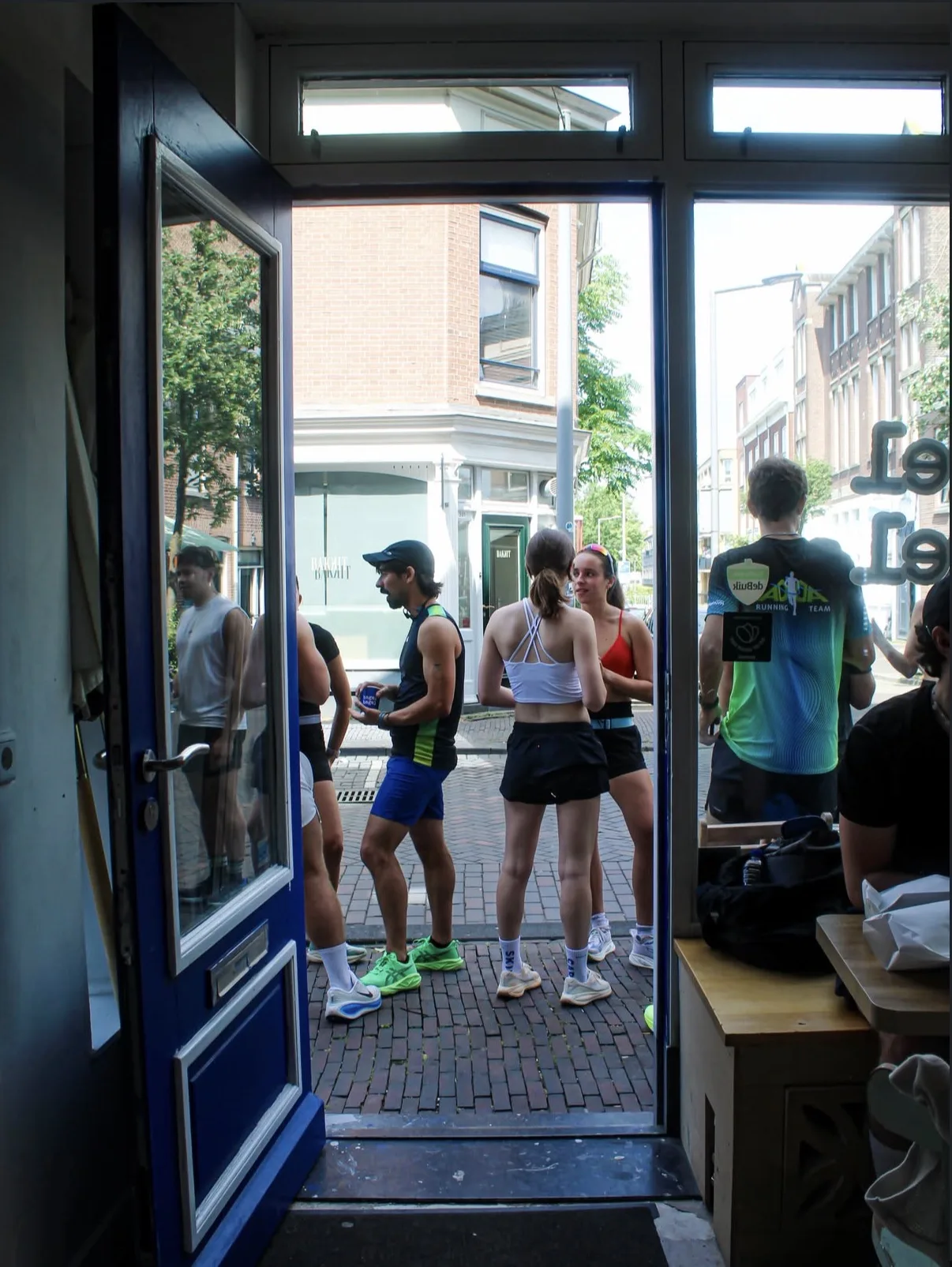 runners chatting on the zwaanshals, seen through the open door of bagel bagel